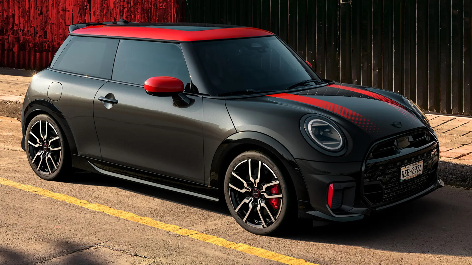 Chili Red renginde tavan ve ayna kapaklarına sahip, Midnight Black gövde renginde MINI John Cooper Works 3 kapı, yandan görünüm, caddede park halinde.